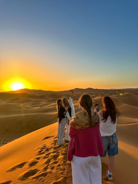 Silhouettes of female friends sitting on a desert dune watching the sunset.