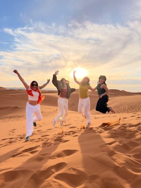 Four happy traveler women jumping on a sand dune at sunset during their 2 day desert tour from marrakech.