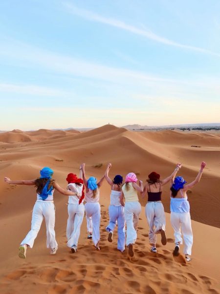 Group of women experiencing a magical sunset in the golden Sahara dunes of Morocco